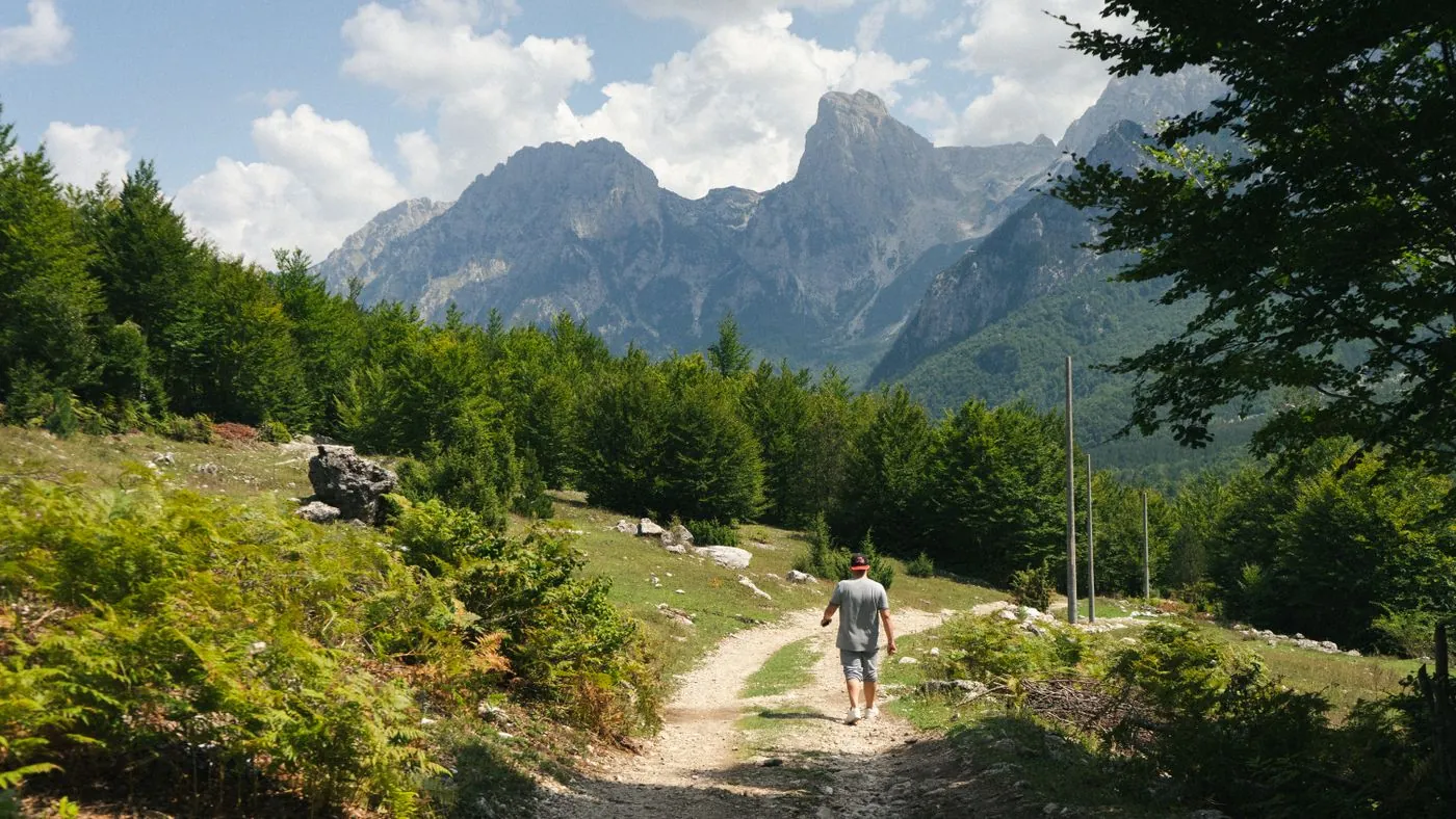 Turista kráčí po cestě pod skalnatými štíty