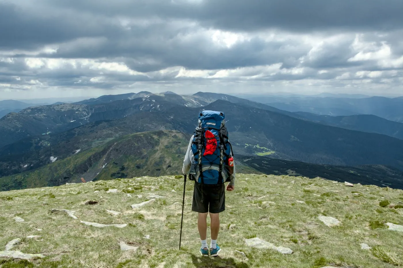 Turista s batohem na hřebeni nad horským údolím