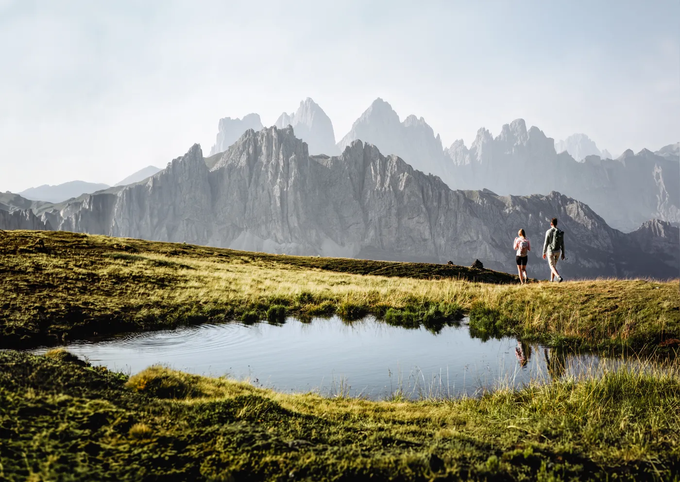 Turisté na horské louce pod skalními štíty Dolomit