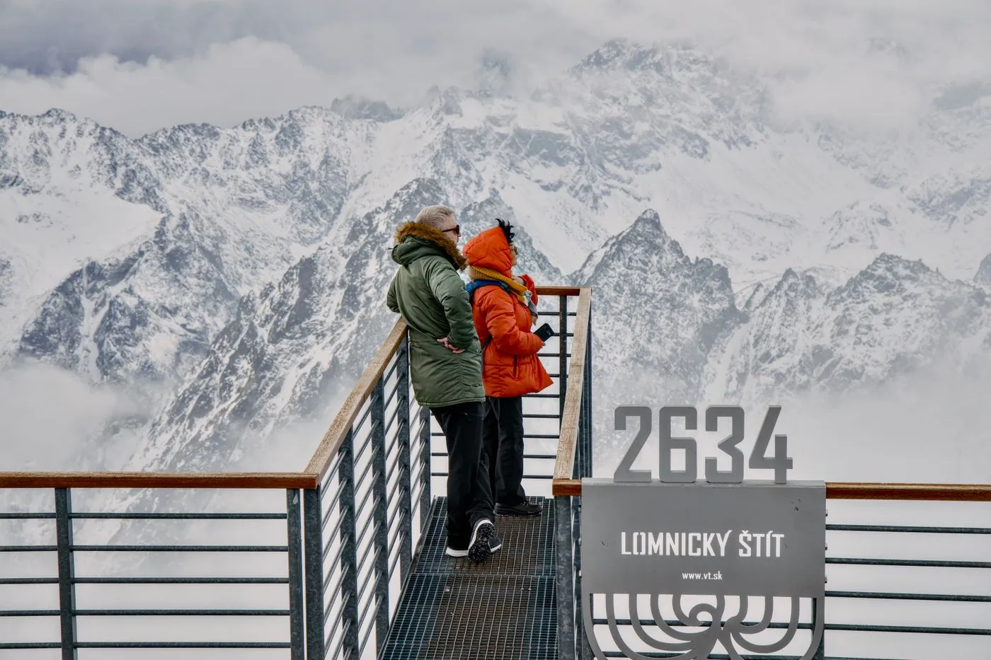 Turisté na vyhlídkové plošině s cedulí Lomnický štít